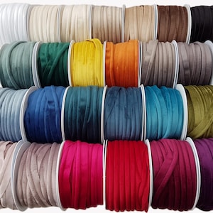 May include: A collection of twenty-four individual spools of velvet ribbon arranged in a grid. The spools feature a variety of colors including white, beige, brown, black, green, yellow, orange, gray, blue, teal, olive, pink, red, and purple.