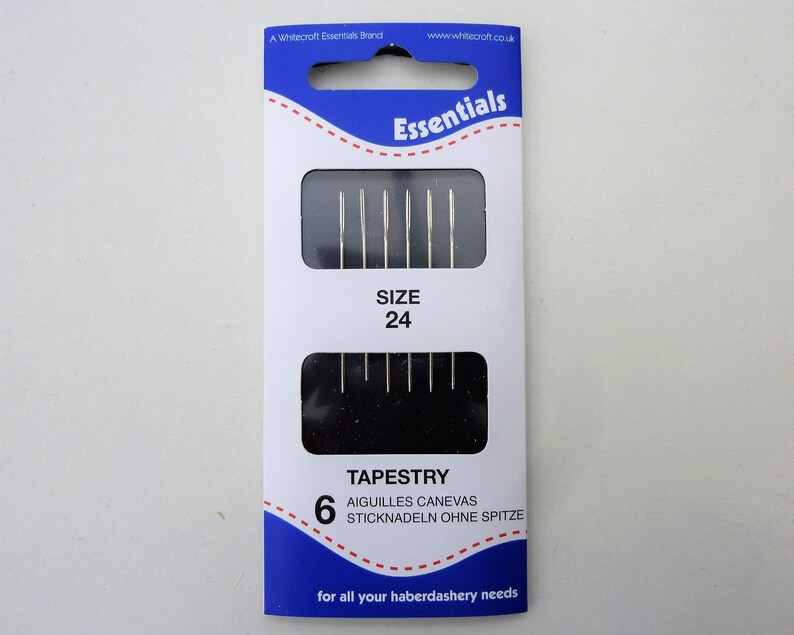 May include: A package of 6 tapestry needles, size 24, in a blue and white package with the text "Essentials" and "TAPESTRY" on it. The package also includes the text "AIGUILLES CANEVAS" and "STICKNADELN OHNE SPITZE".