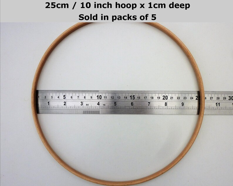 May include: A 10 inch wooden embroidery hoop with a 1 cm depth. The hoop is measured with a ruler. The text "25cm / 10 inch hoop x 1cm deep Sold in packs of 5" is visible at the top of the image.