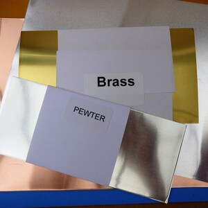K&ouml;nnte beinhalten: Nahaufnahme von vier Metallblechen mit den Beschriftungen "Brass", "Pewter" und "Copper". Die Bleche sind &uuml;bereinander gestapelt, wobei das Messingblech oben liegt, gefolgt vom Zinnblech, dem Kupferblech und einem blauen Blech unten.