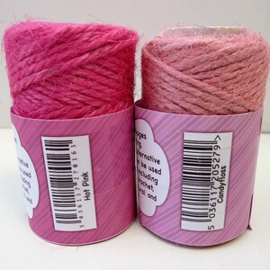 May include: Two spools of pink jute twine, one a darker hot pink and the other a lighter candy floss pink. Both spools have barcodes and product information labels.