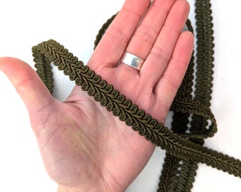 May include: Olive green decorative trim with a looped edge design. The trim is made of a woven material and is shown in a close-up view. The trim is approximately 0.5 inches wide and is suitable for various craft projects.