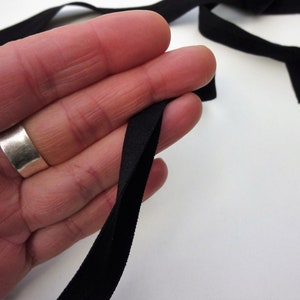 Puede incluir: Cinta el&aacute;stica negra doblada por la mitad, sostenida en una mano. La cinta tiene aproximadamente 2,5 cm de ancho.
