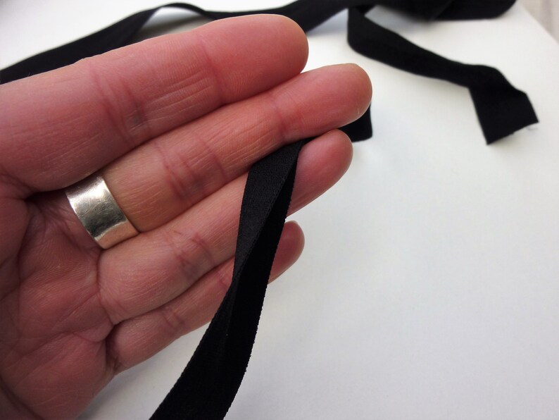 Puede incluir: Cinta el&aacute;stica negra doblada por la mitad, sostenida en una mano. La cinta tiene aproximadamente 2,5 cm de ancho.