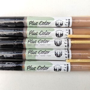 May include: Five brown and black markers with a green and white label that says "Plus Color" and "Marker | Marker | Feutres | Tusch". The label also has a black and white logo with the text "Shake Before Use" and "Kreativ".