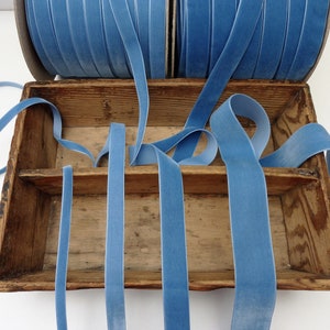 May include: A wooden box filled with multiple spools of light blue velvet ribbon. The ribbon is arranged in a criss-cross pattern.