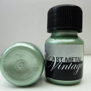 K&ouml;nnte beinhalten: Zwei Flaschen metallisch gr&uuml;ner Farbe mit schwarzem Deckel und einem Etikett mit der Aufschrift "Art Metal Vintage".