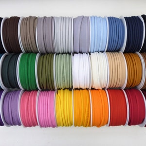 May include: A selection of colourful bias tape spools in a variety of shades, including black, brown, grey, blue, green, yellow, and red. The tape is neatly wound on white spools, offering a wide range of colours for sewing and crafting projects.
