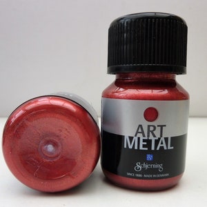 K&ouml;nnte beinhalten: Zwei Flaschen roter Metallic-Farbe mit der Aufschrift "Art Metal" von Schjerning. Die Flaschen werden in D&auml;nemark hergestellt und haben eine leuchtende rote Farbe.