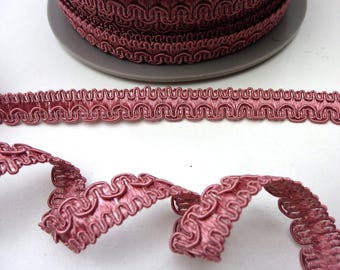 Könnte beinhalten: Mauvefarbene Borte mit einer geschlungenen Kante, in einer Rolle und ausgerollt dargestellt. Das detaillierte Muster der Borte ist sichtbar. Diese Borte eignet sich zum Verzieren von Kleidung, Accessoires oder Heimdekorationsprojekten.