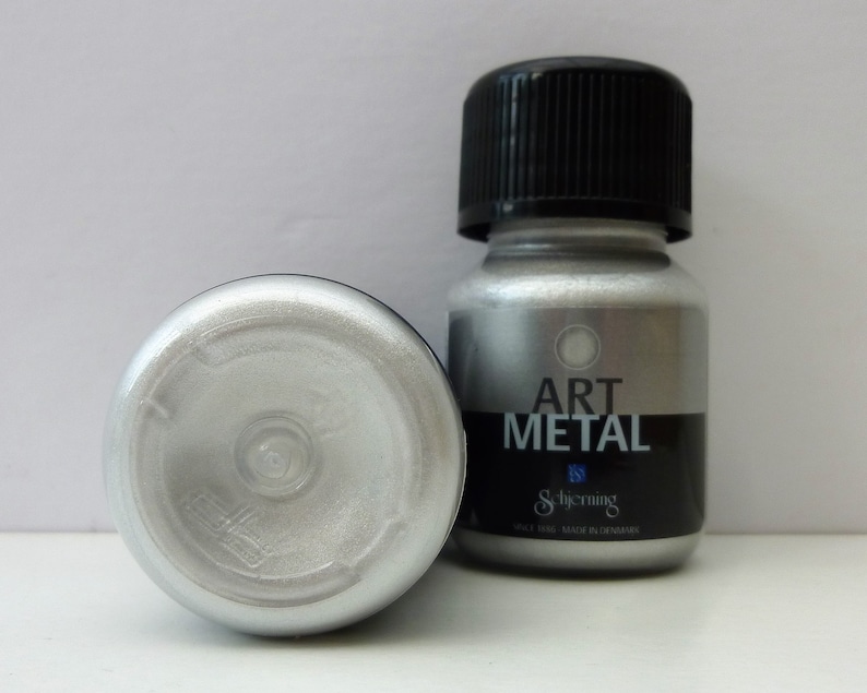 K&ouml;nnte beinhalten: Eine kleine Flasche silberner Metallic-Farbe mit der Aufschrift "Art Metal" von Schjerning. Die Flasche wird in D&auml;nemark hergestellt.