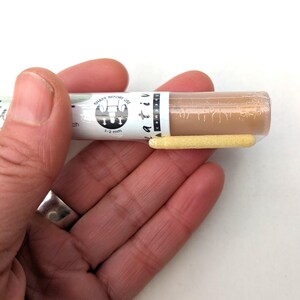 May include: A close-up of a brown paint marker with a white label that says "Shake Before Use" and "1-2 mm". The marker has a yellow tip.