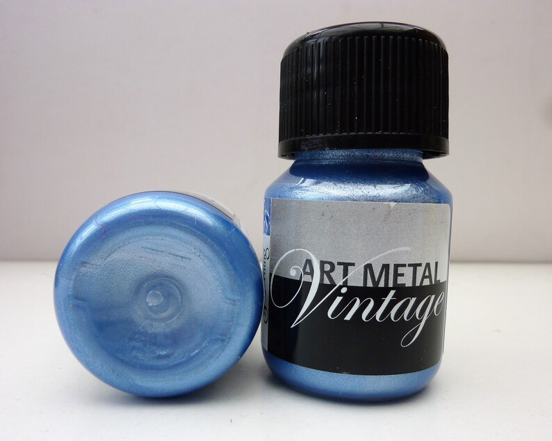 K&ouml;nnte beinhalten: Zwei kleine Flaschen mit blauer Metallic-Farbe und schwarzen Deckeln. Das Etikett auf einer Flasche lautet "Art Metal Vintage".