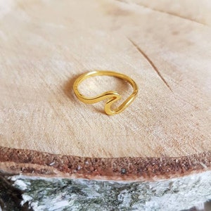 Könnte beinhalten: Ein goldfarbener Wellenring. Der Ring besteht aus einem dünnen Metallband und hat ein schlichtes Wellendesign.