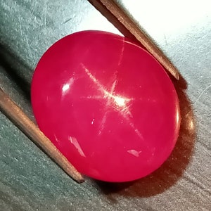 Könnte beinhalten: Ein leuchtend rosa Sternrubin-Edelstein mit einem sechszackigen Stern in der Mitte.