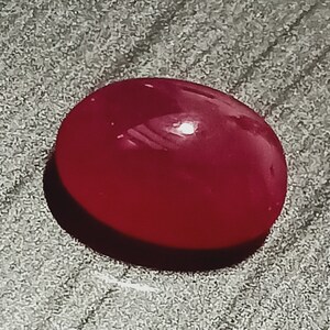 Könnte beinhalten: Ein glatter, ovaler, roter Edelstein mit hohem Glanz.