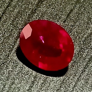 Può includere: Una pietra preziosa ovale di colore rosso intenso con una superficie liscia e lucida.