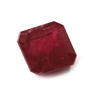 Puede incluir: Una piedra preciosa de color rojo intenso con forma rectangular facetada.