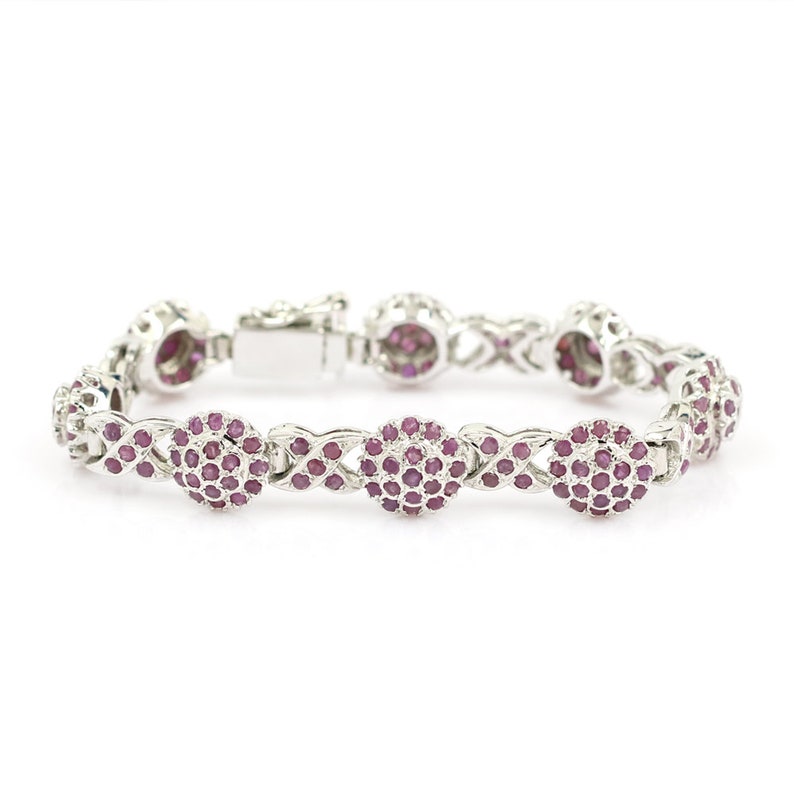 May include: A silver bracelet with a delicate chain design and round pink gemstones. The bracelet has a clasp closure.