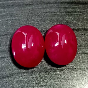 May include: Two oval-shaped, bright pink gemstones. The gemstones are smooth and shiny.