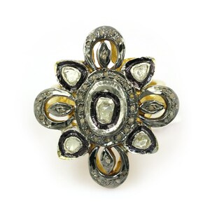 May include: A gold ring with a floral design featuring a central oval-shaped stone surrounded by smaller stones. The ring is set with diamonds and has a black oxidized finish.