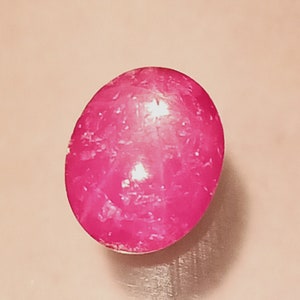 May include: A pink oval-shaped gemstone with a smooth, polished surface. The stone has a slight sparkle and a light pink hue.