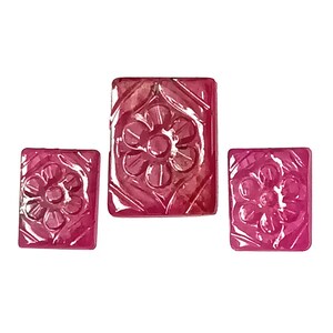 Puede incluir: Tres piedras preciosas de rubí talladas, cada una con un diseño floral. Las piedras preciosas son rectangulares y tienen un color rojo intenso.