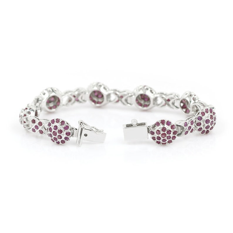 May include: A silver bracelet with a delicate chain design and round red ruby accents. The bracelet is open and ready to be worn.
