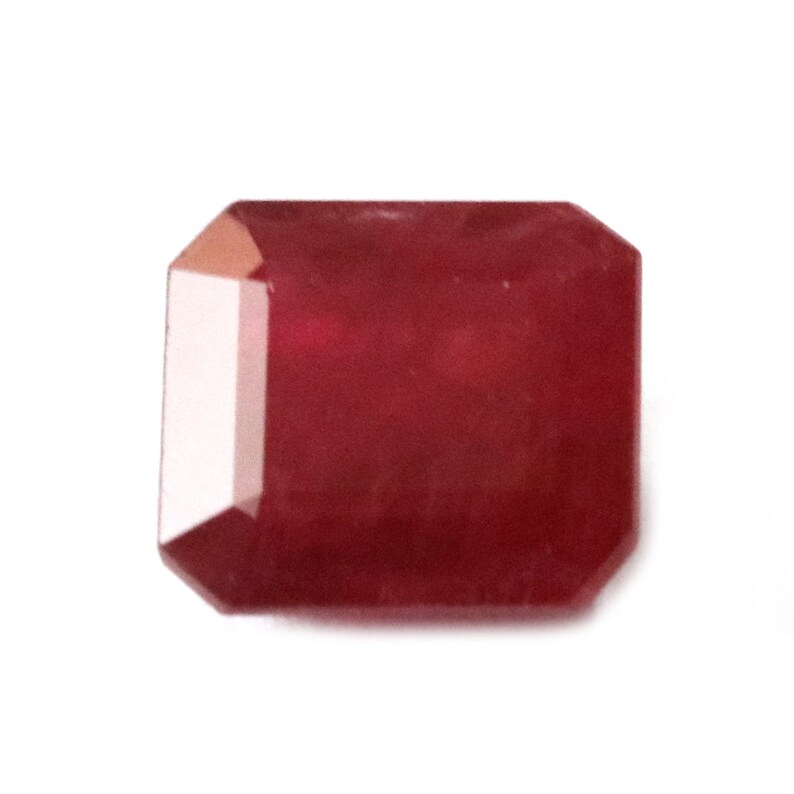 Puede incluir: Una piedra preciosa de color rojo intenso con forma rectangular y una superficie lisa y pulida.