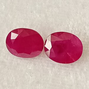 May include: Two oval-shaped, faceted ruby gemstones. The rubies are a deep, rich red colour.