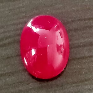 May include: A bright pink oval-shaped cabochon gemstone.