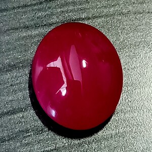 May include: A round, bright red cabochon gemstone with a smooth, polished surface.