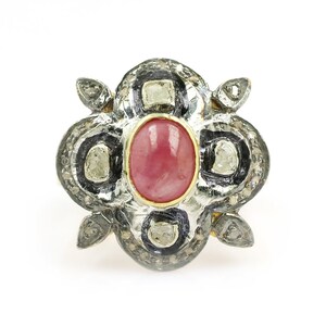 Puede incluir: Un anillo de plata con una piedra preciosa rosa rodeada de diamantes más pequeños. El anillo tiene un diseño floral.