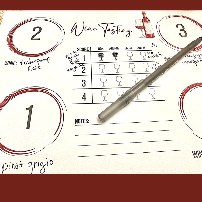 May include: A white wine tasting scorecard with three wines listed: Pinot Grigio, Vanderpump Rose, and an unnamed wine. The scorecard has categories for look, aroma, taste, finish, and a 9/10 rating system. A pen is lying on top of the scorecard.
