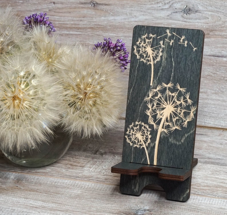Pu&ograve; includere: Un supporto per telefono in legno grigio scuro con un'apertura per un telefono. Il supporto &egrave; decorato con un design di fiori di tarassaco tagliato al laser.
