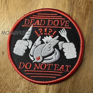 May include: Round black patch with red trim featuring the text "DEAD DOVE DO NOT EAT" in red. A white dove is in the center, with a knife and fork on either side. The brand name "MOSSFUZZ" is in the upper left corner.