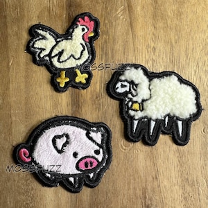 以下が含まれることがあります： 白い鶏、白い羊、ピンクの豚の刺繍パッチが3つ。パッチはすべて黒で縁取られており、ふわふわした質感です。