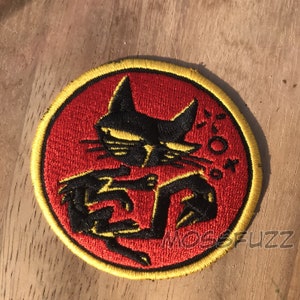 May include: A red and yellow embroidered patch with a black cat silhouette. The cat is in a fighting pose with its claws out. The text "'50'" is embroidered in yellow on the patch.