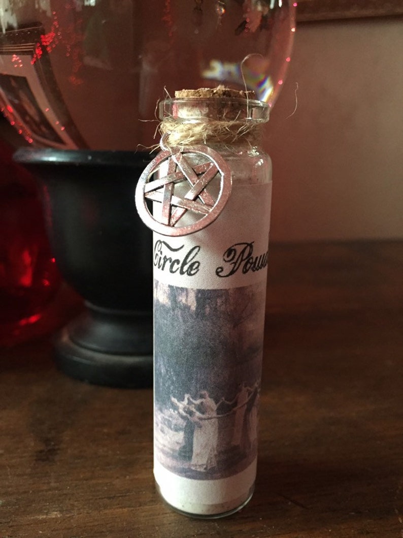 May include: A small glass bottle with a cork stopper and a silver pentagram charm. The bottle is labeled "Circle Power" and has a black and white image of a group of people holding hands in a circle.