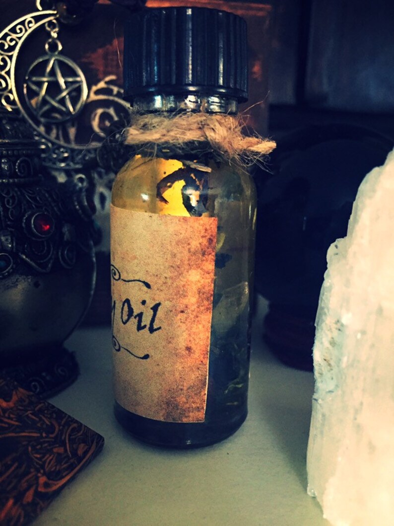 May include: A small glass bottle with a brown label that says "Oil" on it. The bottle is filled with a clear liquid and has a black cap. The bottle is sitting on a white surface.