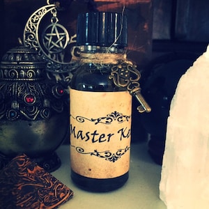 May include: A small brown glass bottle with a black lid and a label that says "Master Key". The bottle is tied with twine and has a small key charm attached.