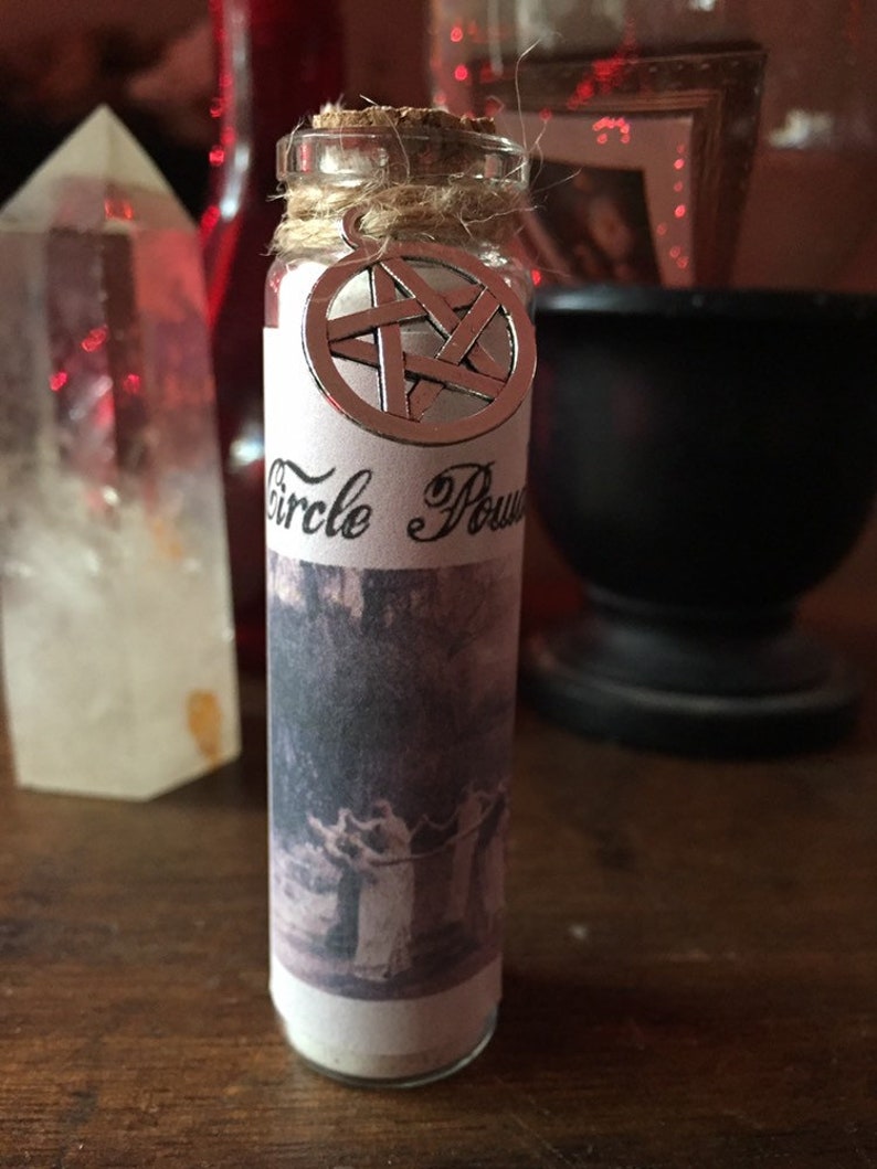 May include: A small glass bottle with a cork stopper and a silver pentagram charm. The bottle is labeled "Circle Power" and contains a white powder. The bottle is sitting on a wooden surface.