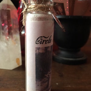 May include: A small glass bottle with a cork stopper and a twine closure. The bottle is filled with a white powder and has a label that says "Circle of".