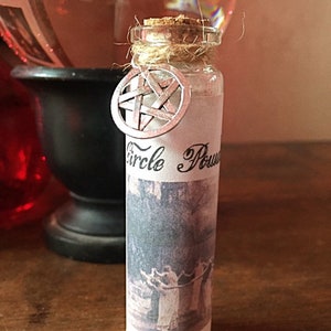 May include: A small glass bottle with a cork stopper and a white label that reads "Circle Power". The bottle is tied with twine and has a silver pentagram charm attached.