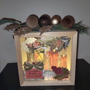 May include: A wooden box with a Christmas theme. The box contains paper candles, holly leaves, and a bow with the text "Let the lights of Christmas make the season bright." The top of the box is decorated with ornaments and greenery.
