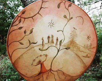 May include: A round, hand-painted drum with a brown leather surface. The drum features a stylized tree with roots, a bird, and five figures standing on a hill. The background is a soft pink with a sun-like symbol.