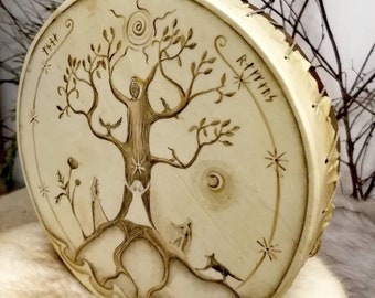 May include: A white leather drum with a hand-painted design of a tree of life with birds, a moon, and stars. The drum is surrounded by a circle of runes and the word "Rhythms" is written on the side.