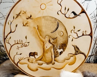 May include: A hand-painted leather drum with a depiction of a woman reaching up to the sun and moon. The drum also features birds, trees, and other animals.