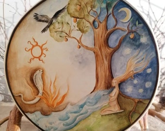 May include: A round wooden plate with a watercolor painting of a tree with a bird, a snake, a sun, a moon, and a woman. The tree has green leaves and brown branches. The woman is sitting on the ground with her hair flowing in the wind. The snake is coiled around a fire. The sun is in the upper left corner of the plate. The moon is in the upper right corner of the plate.