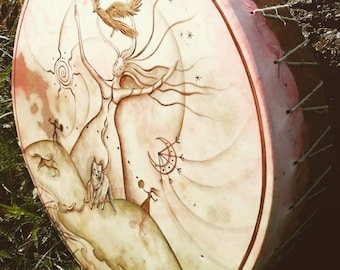 May include: A hand-painted drum with a pink and brown design. The drum features a woman with outstretched arms, a bird flying above her, and a wolf standing on a hill. The drum is surrounded by a decorative border.